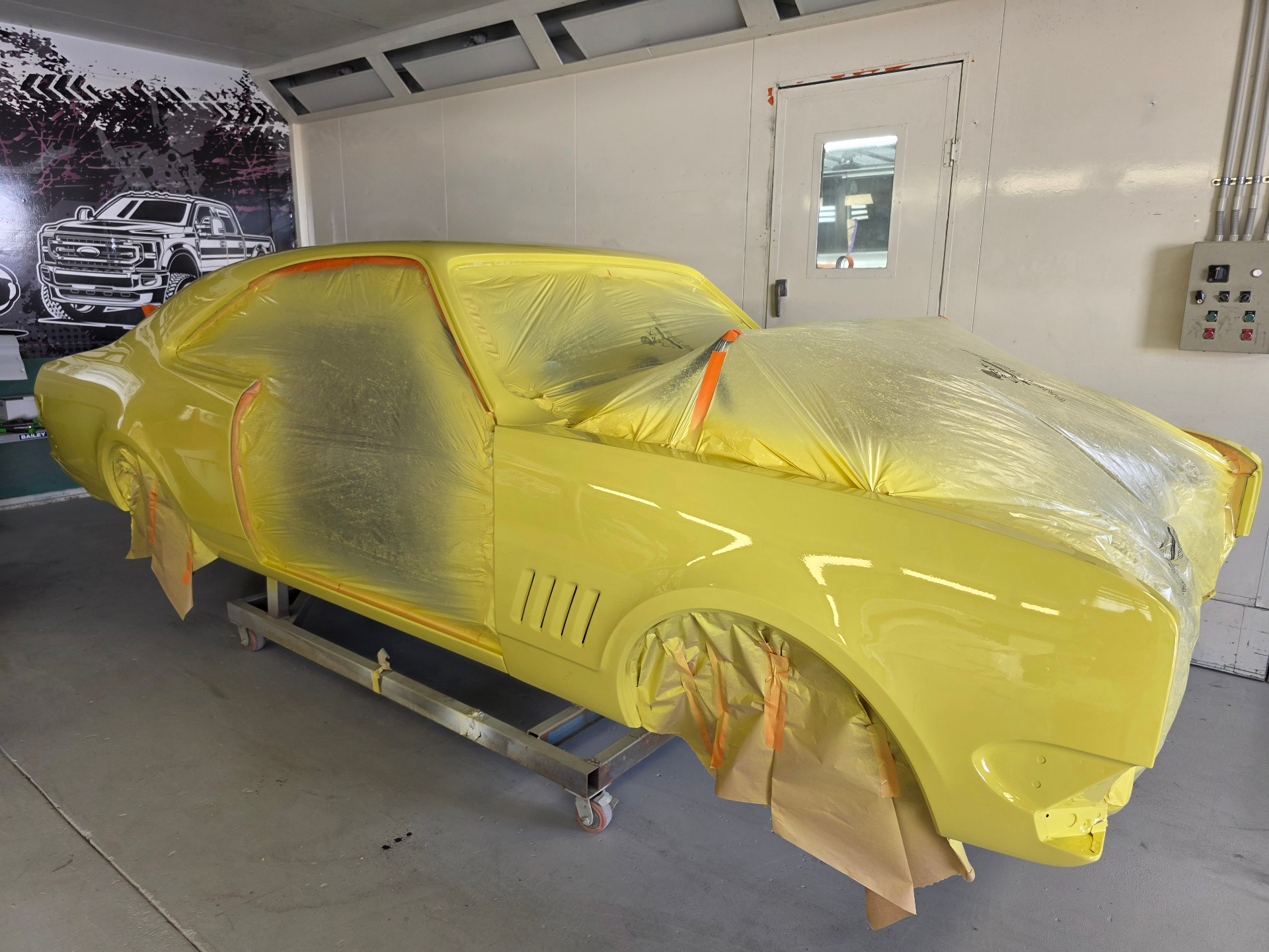 Yellow muscle car mid-paint in the booth, masked
